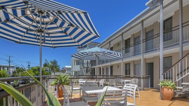 Une terrasse d’hôtel avec des sièges en plein air, des parasols à rayures et des plantes en pot.