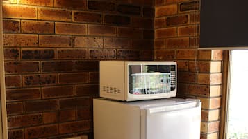 A compact kitchen with a brick wall, a white refrigerator, and a microwave on top.