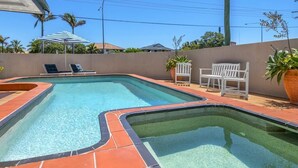 Une piscine dotée d’une terrasse carrelée, de chaises longues et d’une pergola surmontée d’auvents à rayures.