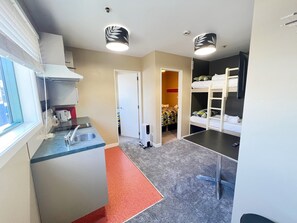 A compact hotel room with a kitchenette, a bed with a bunk, a desk, and a chair. - Astray Motel (Rotorua)