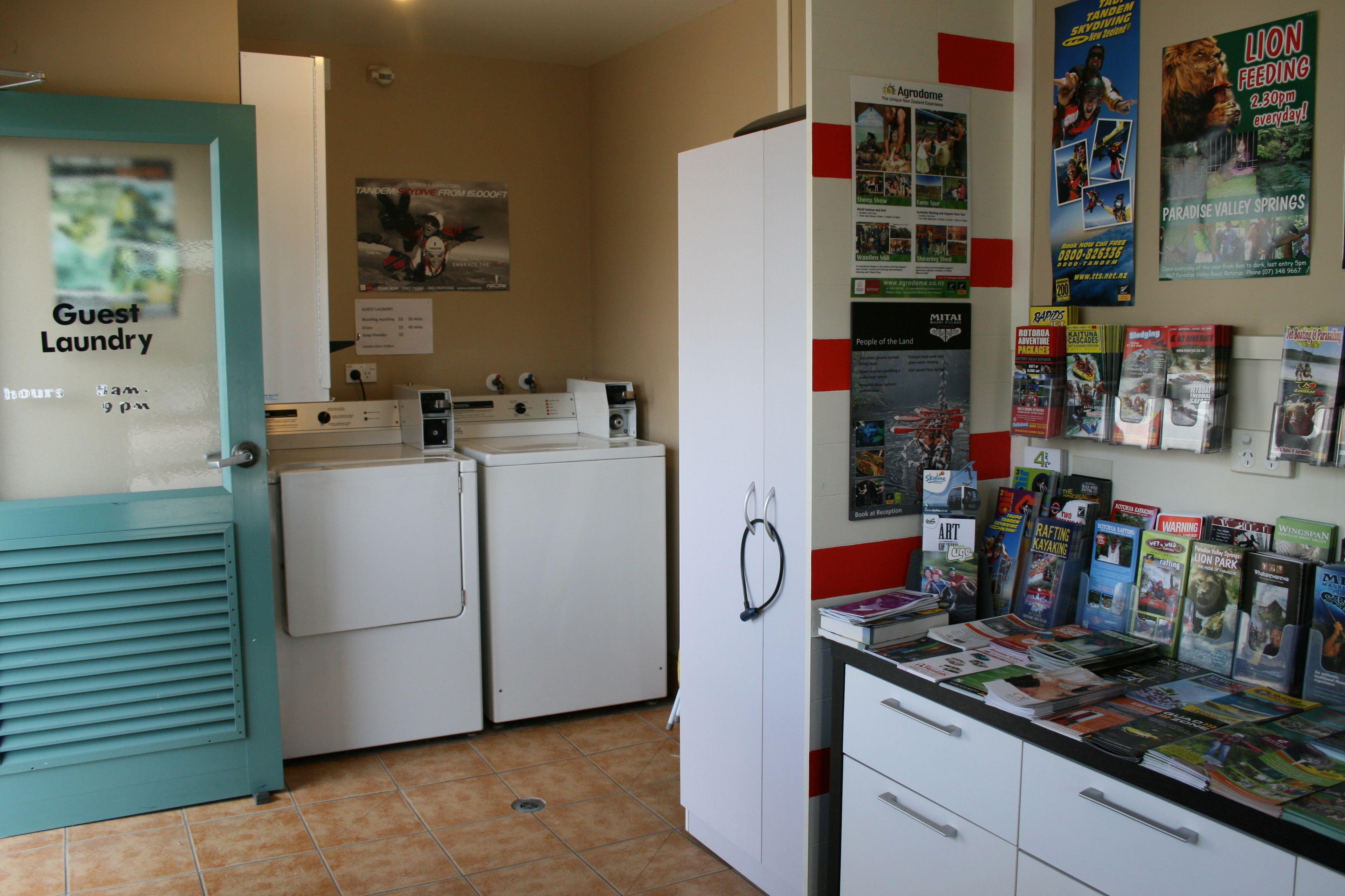 A laundry area with a sign for guest laundry, a bulletin board with travel posters, and a counter with magazines.