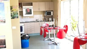 A hotel room with a kitchenette, a dining area with red chairs, a sofa, and a large window with curtains. - Astray Motel (Rotorua)