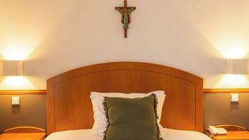 A hotel room with a wooden headboard, a green pillow, white bedding, and a cross on the wall.