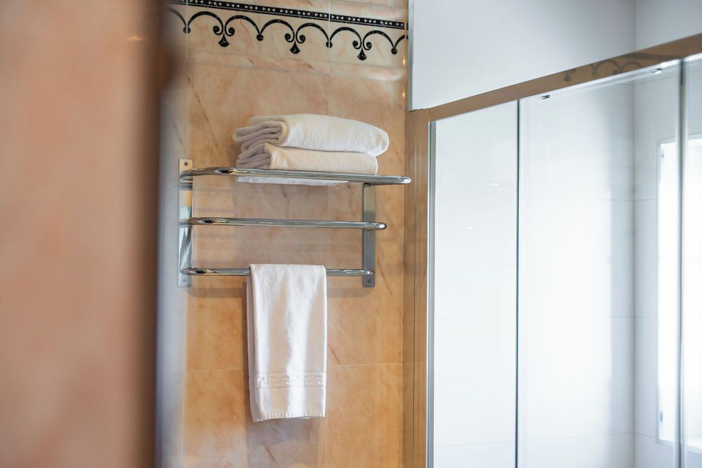 Un baño con pared de mármol, un perchero con toallas dobladas y una puerta de ducha de cristal.