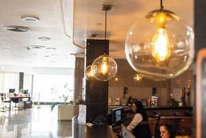 Un área de recepción de hotel moderna con una lámpara de cúpula de cristal, un mostrador de recepción y un monitor de computadora.