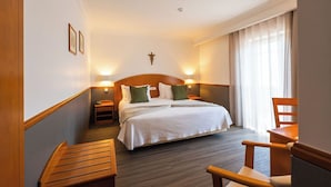 Une chambre d’hôtel avec un grand lit, deux tables de chevet, un banc en bois et une chaise.
