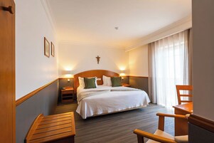 Quarto de hotel com uma cama grande, duas mesas de cabeceira, um banco de madeira e uma cadeira.
