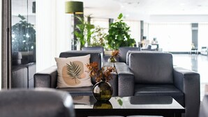 Un hall d’entrée moderne avec un espace salon, un mur en verre et une grande plante.