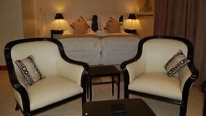 Una habitación de hotel con dos camas individuales, una mesita, dos sillones y dos lámparas de noche.