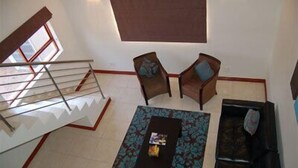 Un amplio salón con una escalera, un sofá, dos sillones y una mesa de centro.