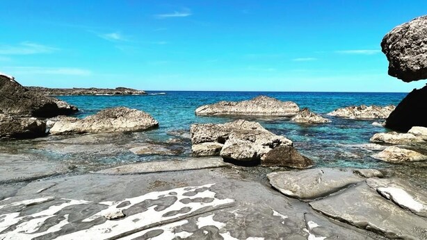 Eine felsige Küstenlinie mit klarem, blauem Wasser und blauem Himmel.