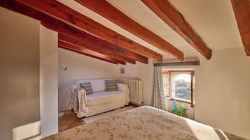 A bedroom with a bed, a sofa, a radiator, a window with curtains, and a view of the outdoors.