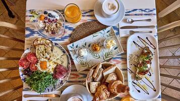 A breakfast setting with various dishes, including eggs, bread, and a croissant, on a table with a patterned tablecloth.