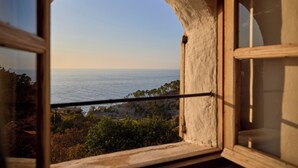 Blick durch ein Rundbogenfenster auf eine Küstenlandschaft mit Bäumen und blauem Himmel.