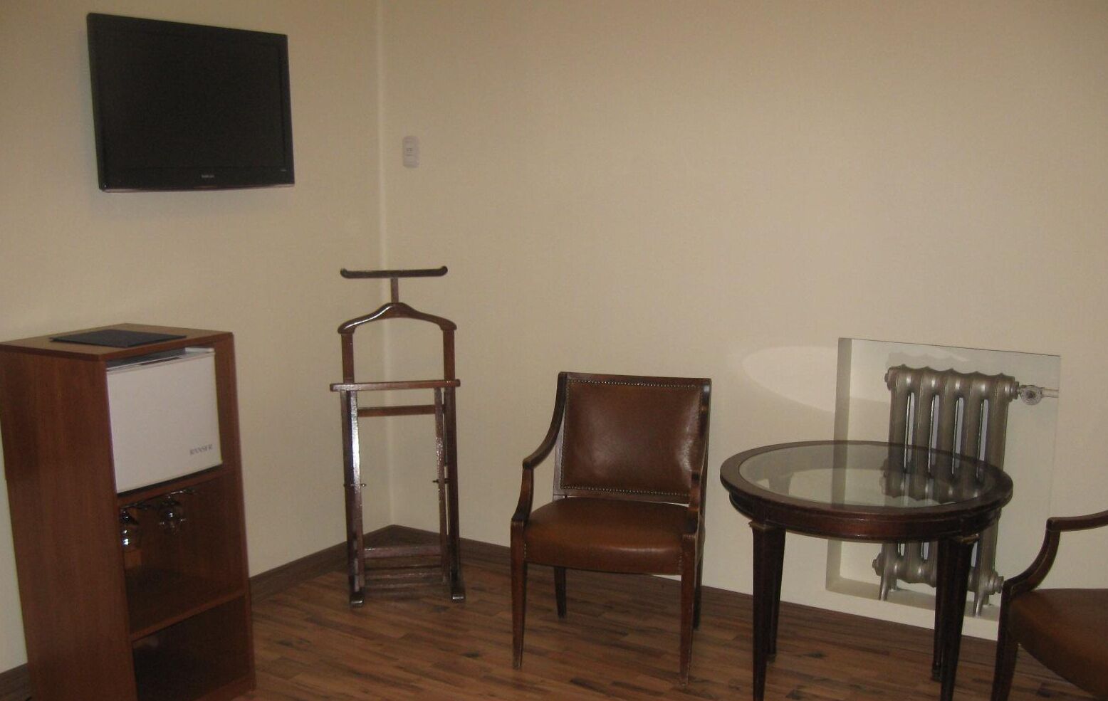 A room with a wooden cabinet, a chair, a glass table, and a radiator.