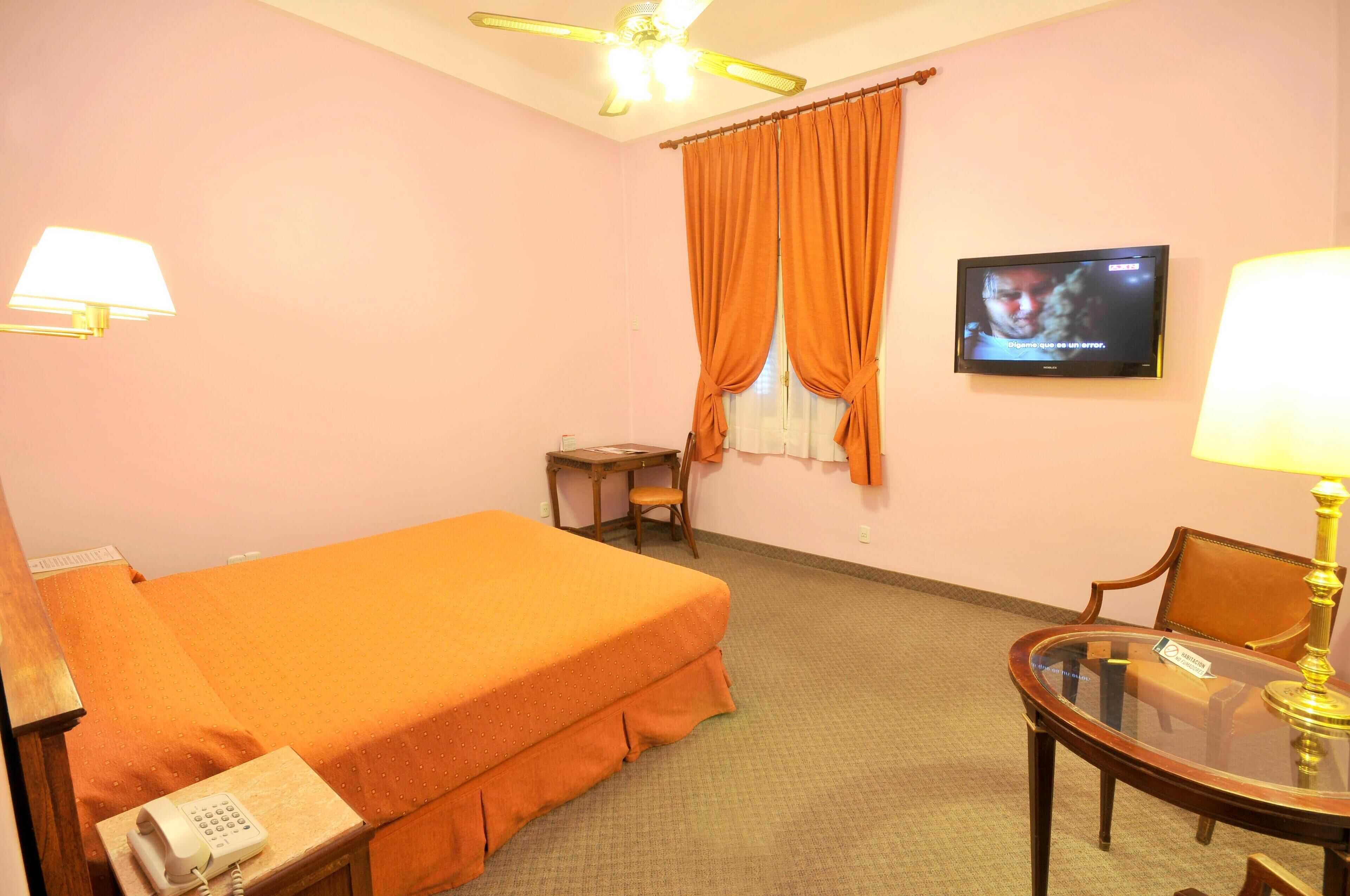 A hotel room with a bed, a desk, a chair, a television, and a telephone.