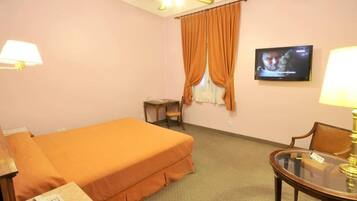 A hotel room with a single bed, a small table, a chair, a television, and a lamp.