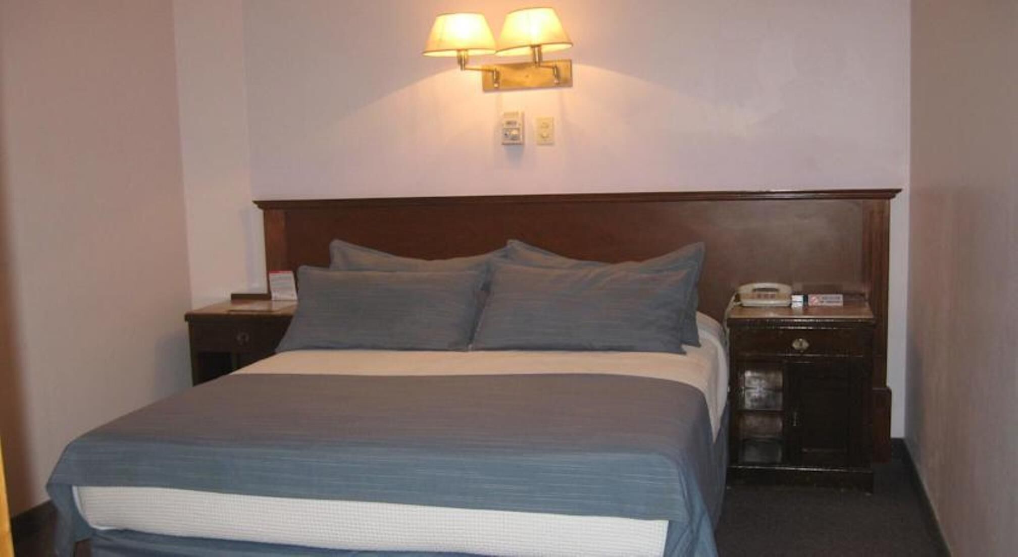 Ein Hotelzimmer mit einem großen Bett, zwei Nachttischen, einer Wandlampe und einem Telefon auf einem der Tische.