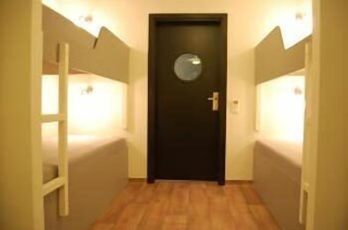 A narrow hallway with a dark door at the end, flanked by walls with light fixtures.