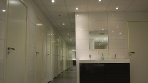 A long hallway with multiple white doors, a modern bathroom with a large sink and mirror, and recessed ceiling lighting. - Hotell Centralstation (Uppsala)