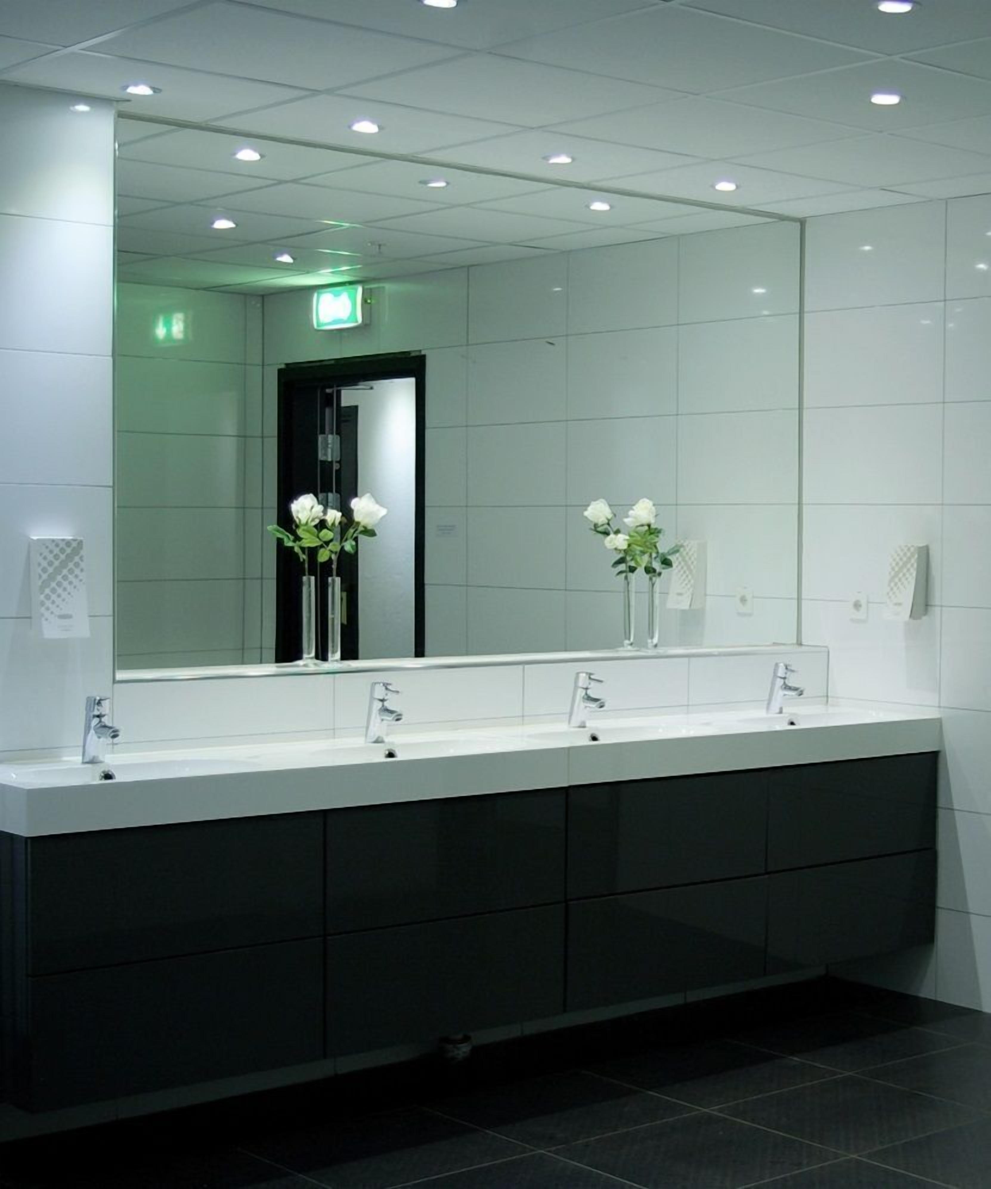 Un baño moderno con tres lavamanos, armarios oscuros y un espejo grande.