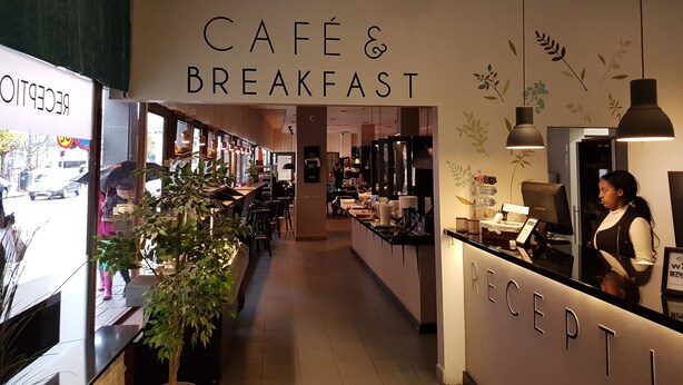 A café & breakfast area with a reception desk, seating, and a plant. - Hotell Centralstation (Uppsala)