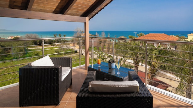 A balcony with wicker furniture, a glass table, and a view of the sea. - Armonia Studios & Apartments (Zakynthos)