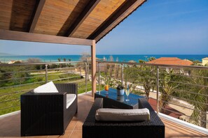 A balcony with wicker furniture, a glass table, and a view of the sea. - Armonia Studios & Apartments (Zakynthos)