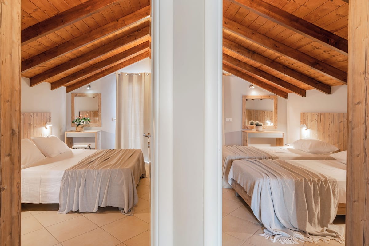 A room with two beds, wooden ceiling beams, a small desk with a chair, and a mirror on the wall.