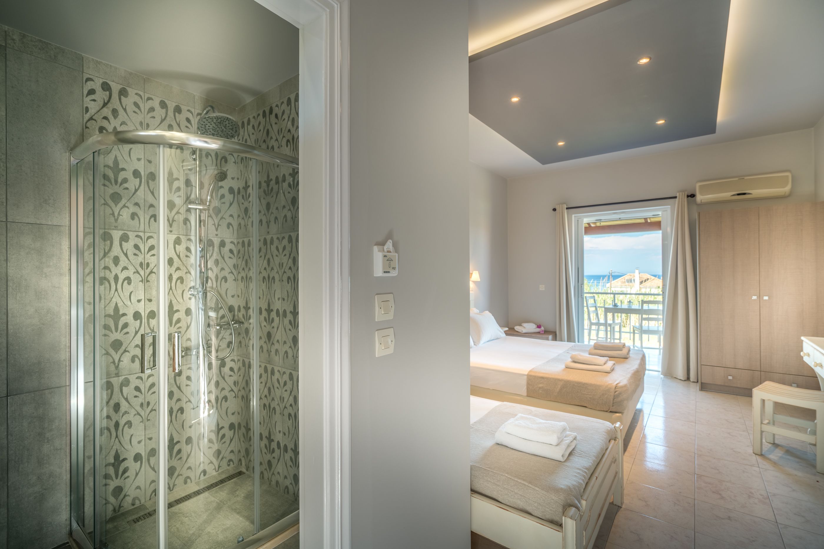 A modern hotel room with a shower, a balcony with a view, and a bed with towels.