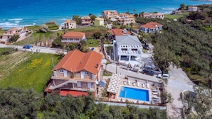 An aerial view of a coastal residential area with houses, a swimming pool, and a view of the sea. - Armonia Studios & Apartments (Zakynthos)