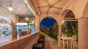 A bar area with a counter, stools, and a seating area with a table and chairs. - Armonia Studios & Apartments (Zakynthos)