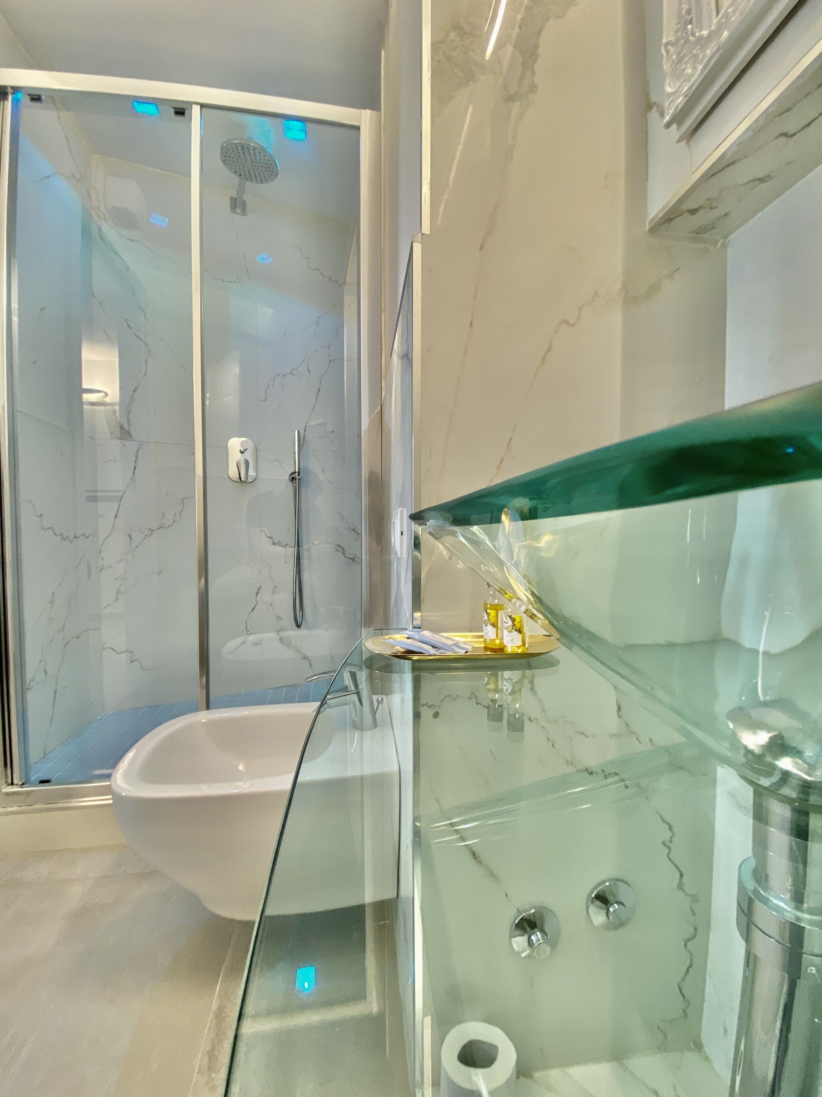 A modern bathroom with a glass shower enclosure, a white bathtub, and a glass vanity with toiletries.