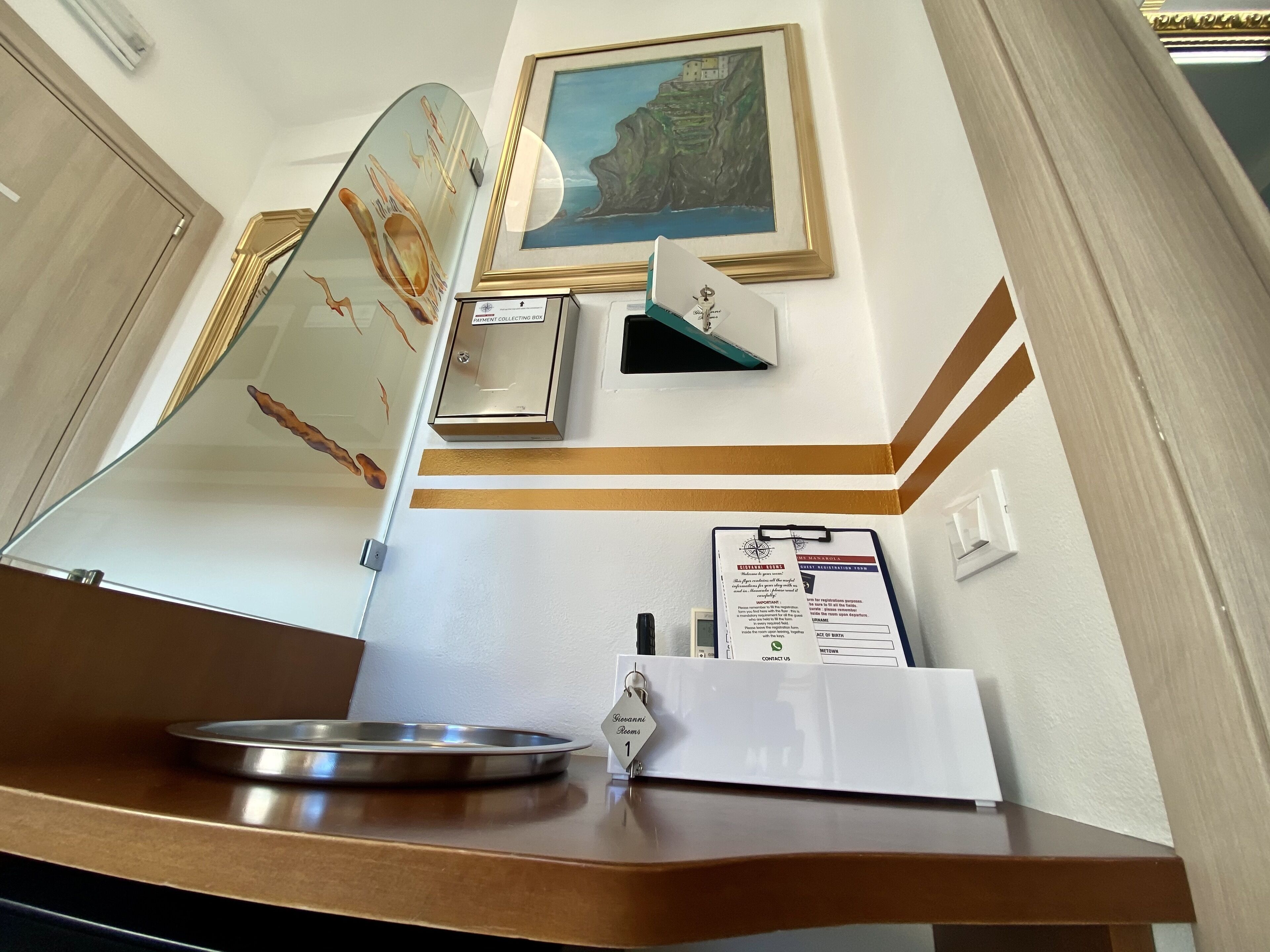 Un comptoir d’accueil orné d’un tableau encadré représentant un paysage côtier, une boîte pour recueillir les paiements et un classeur contenant une carte et des informations.