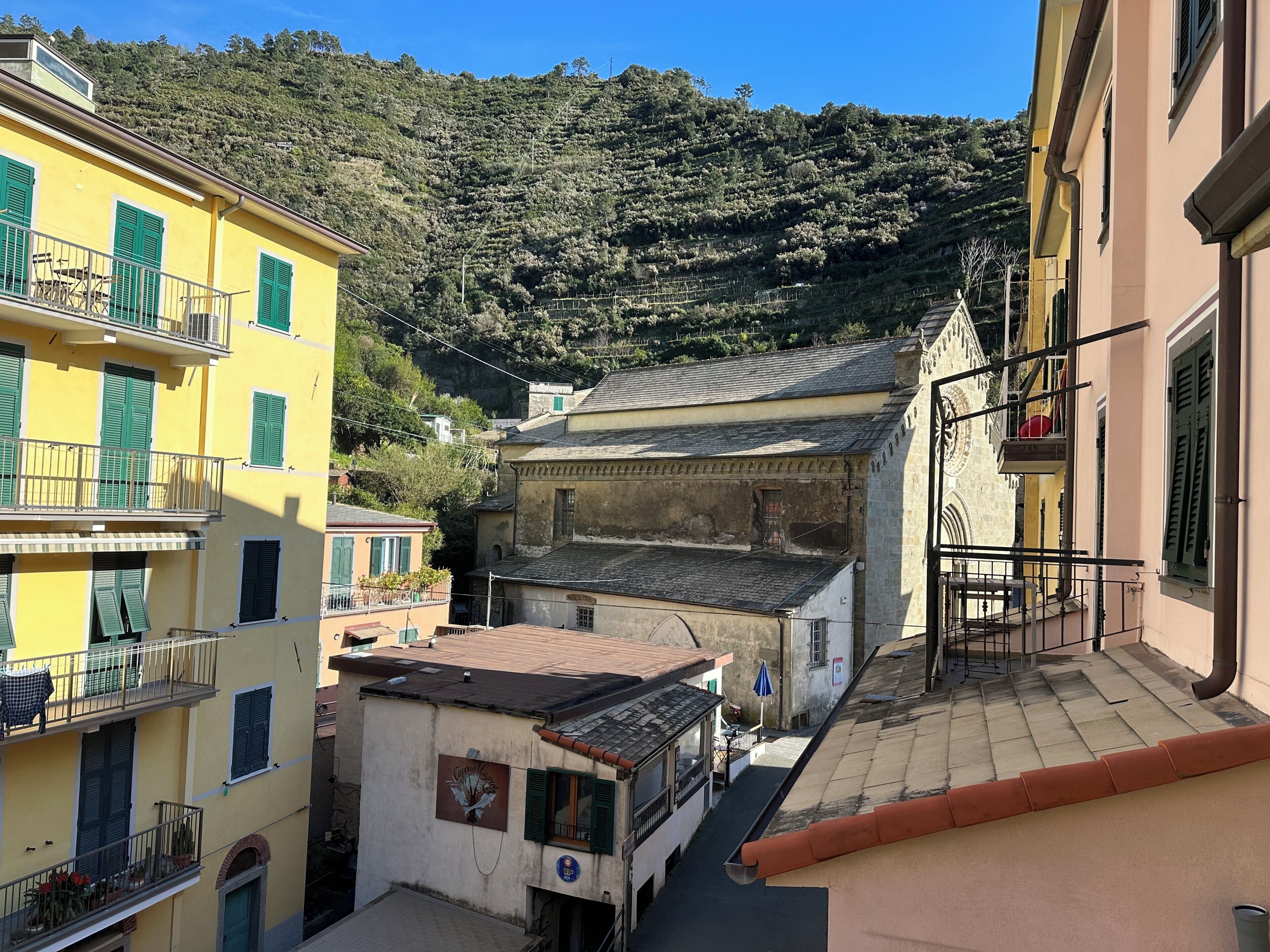 A narrow street with buildings on either side, a mountain in the background, and a clear sky.