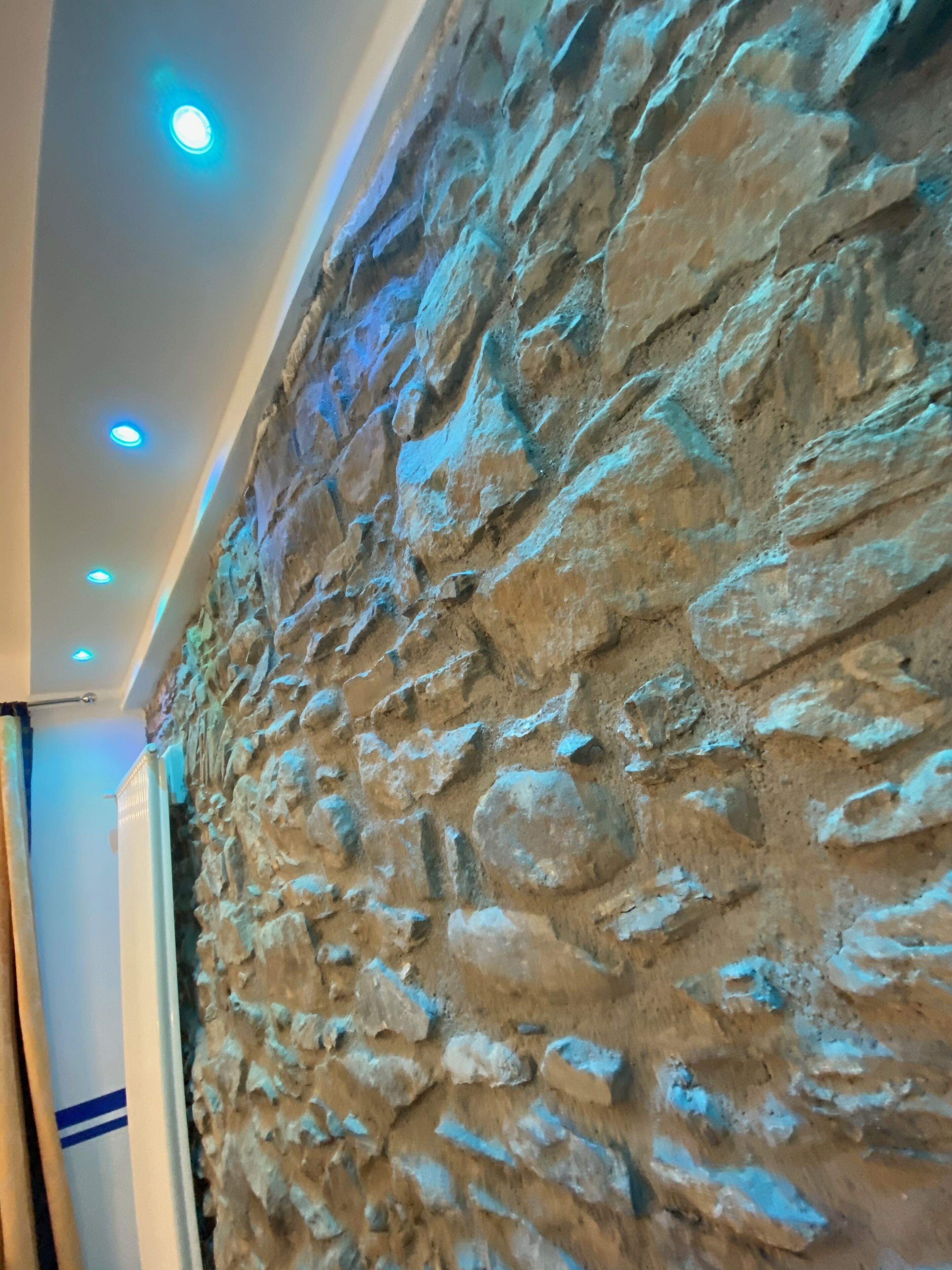 A textured stone wall with a modern ceiling design featuring recessed lighting.