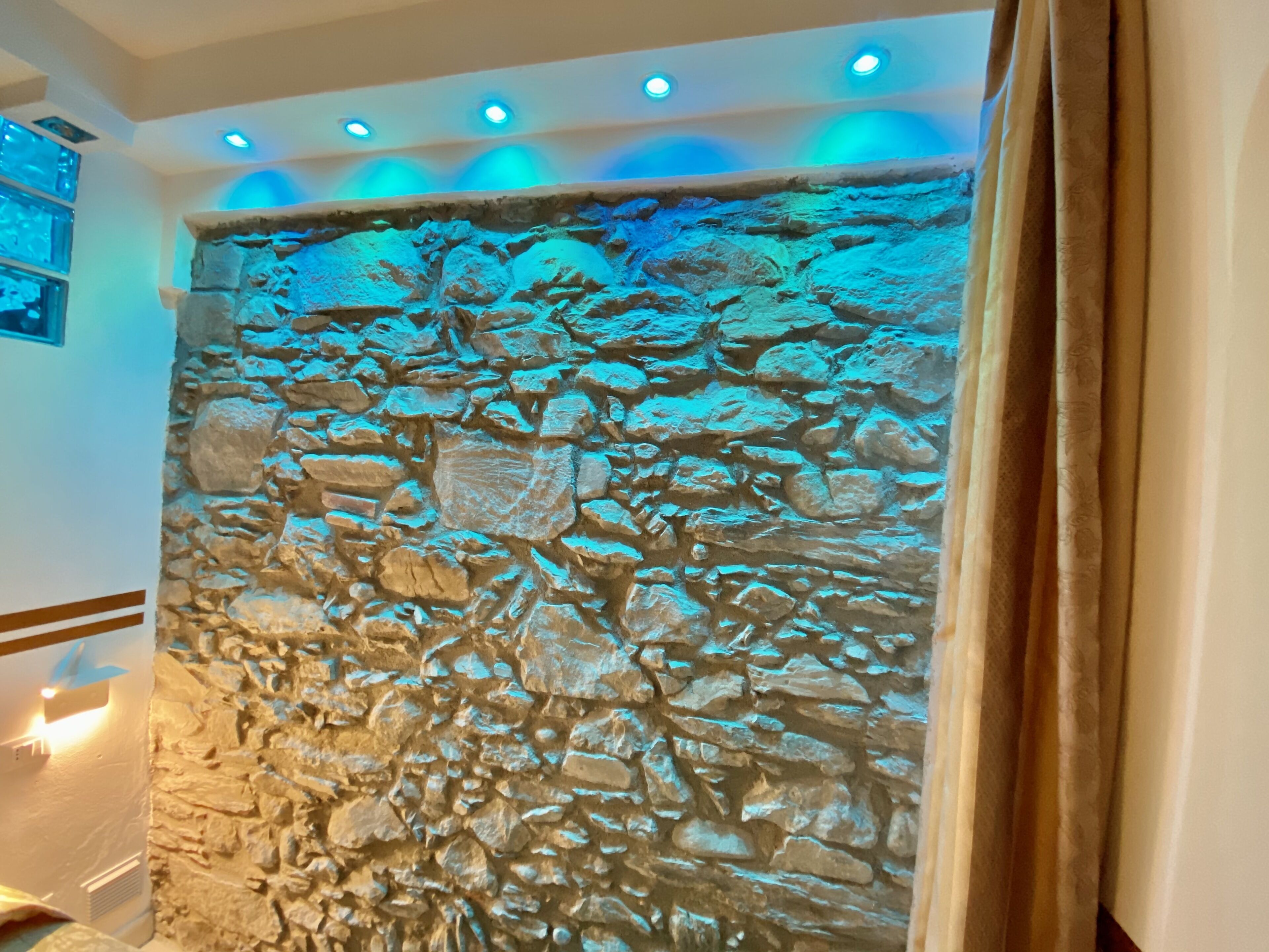 A stone wall with a textured surface, recessed lighting, and a curtain on the right.