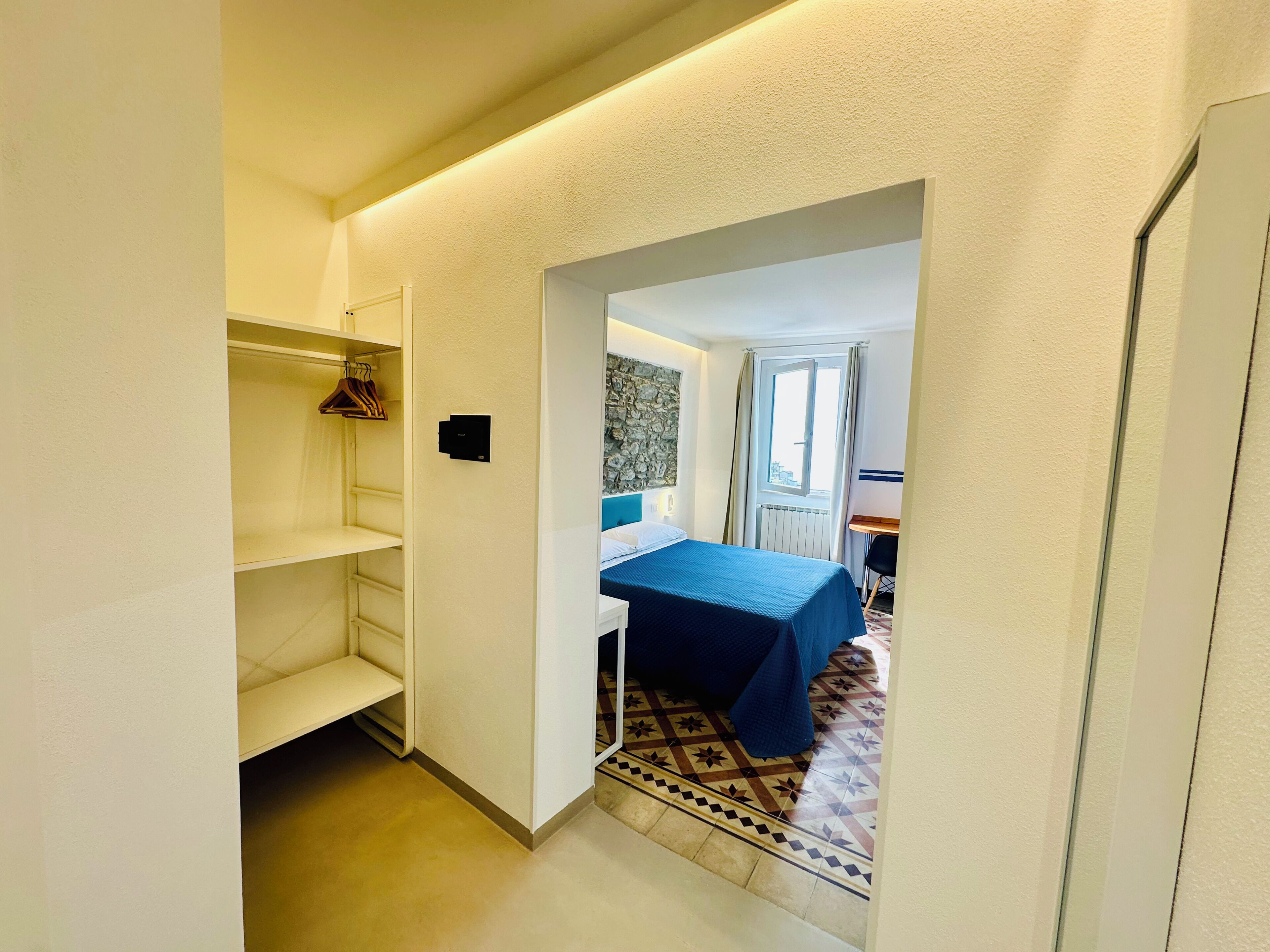 A narrow hallway leading to a bedroom with a bed, a desk, and a radiator.