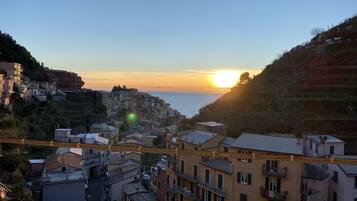 A coastal town with buildings along the hillside, a clear sky, and the sun setting over the sea.