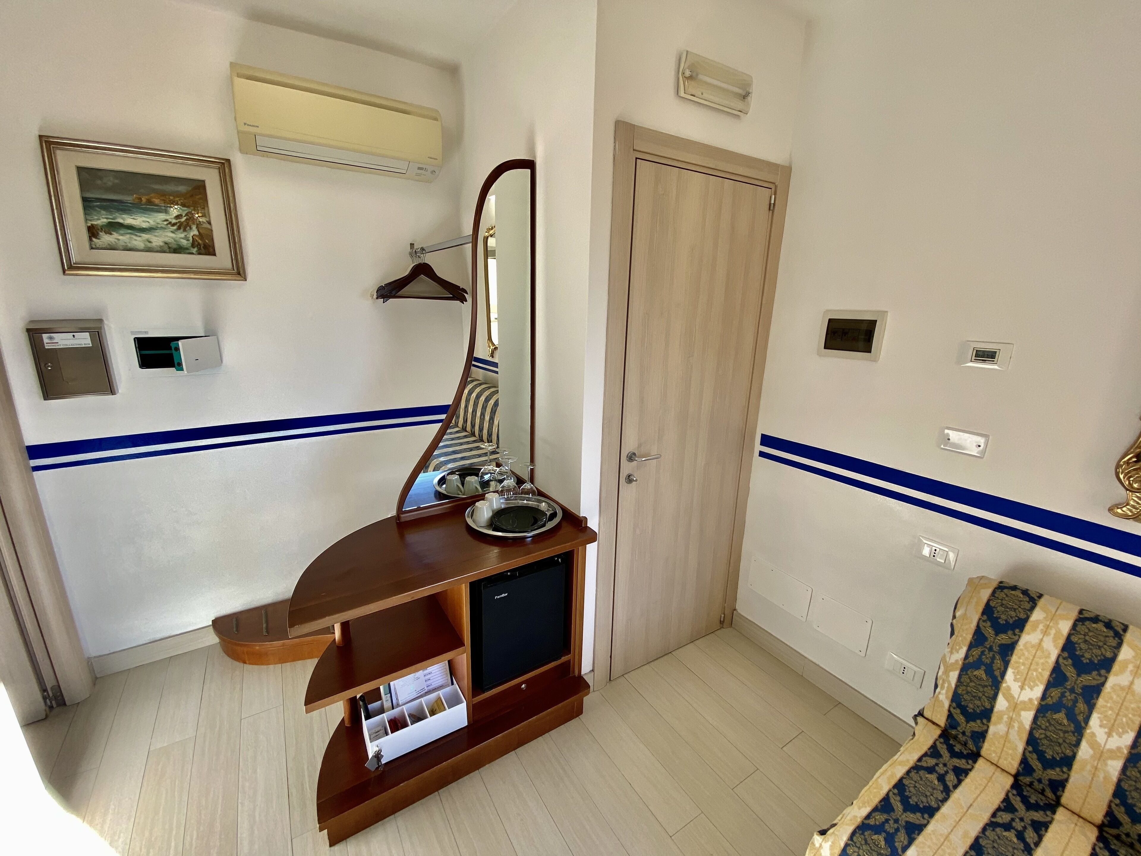 Une chambre d’hôtel avec une console en bois, un lit doté d’une tête de lit à motifs, un miroir et une porte.