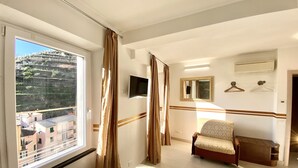 Ett hotellrum med en säng, en stol, en tv och utsikt över byggnaderna utanför fönstret.