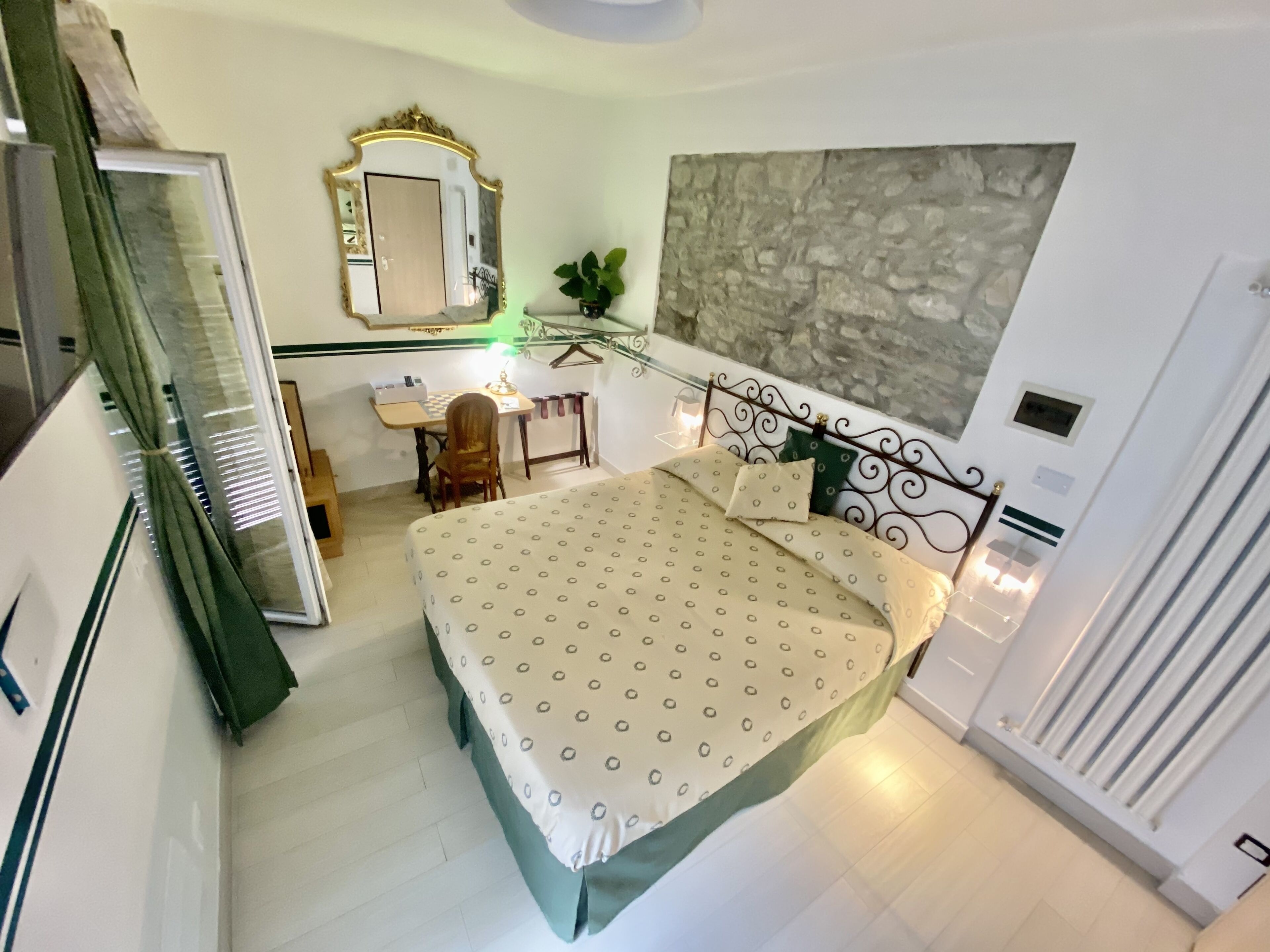 A bedroom with a bed, a desk, a chair, a mirror, and a stone wall.