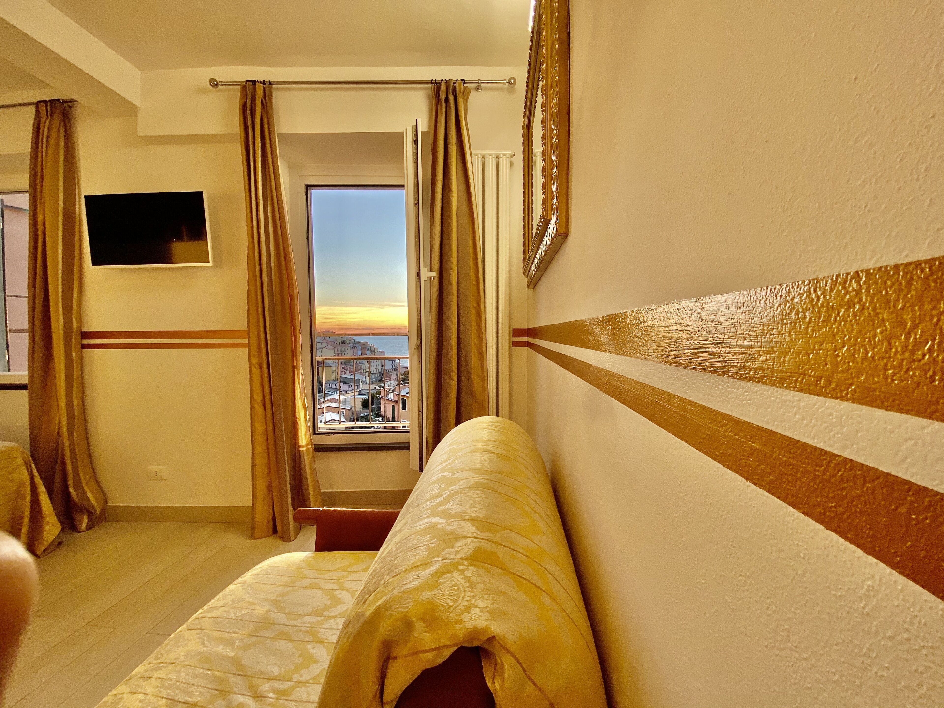 Una habitació d'hotel amb un llit, televisió, finestra amb cortines i vista a un paisatge urbà.