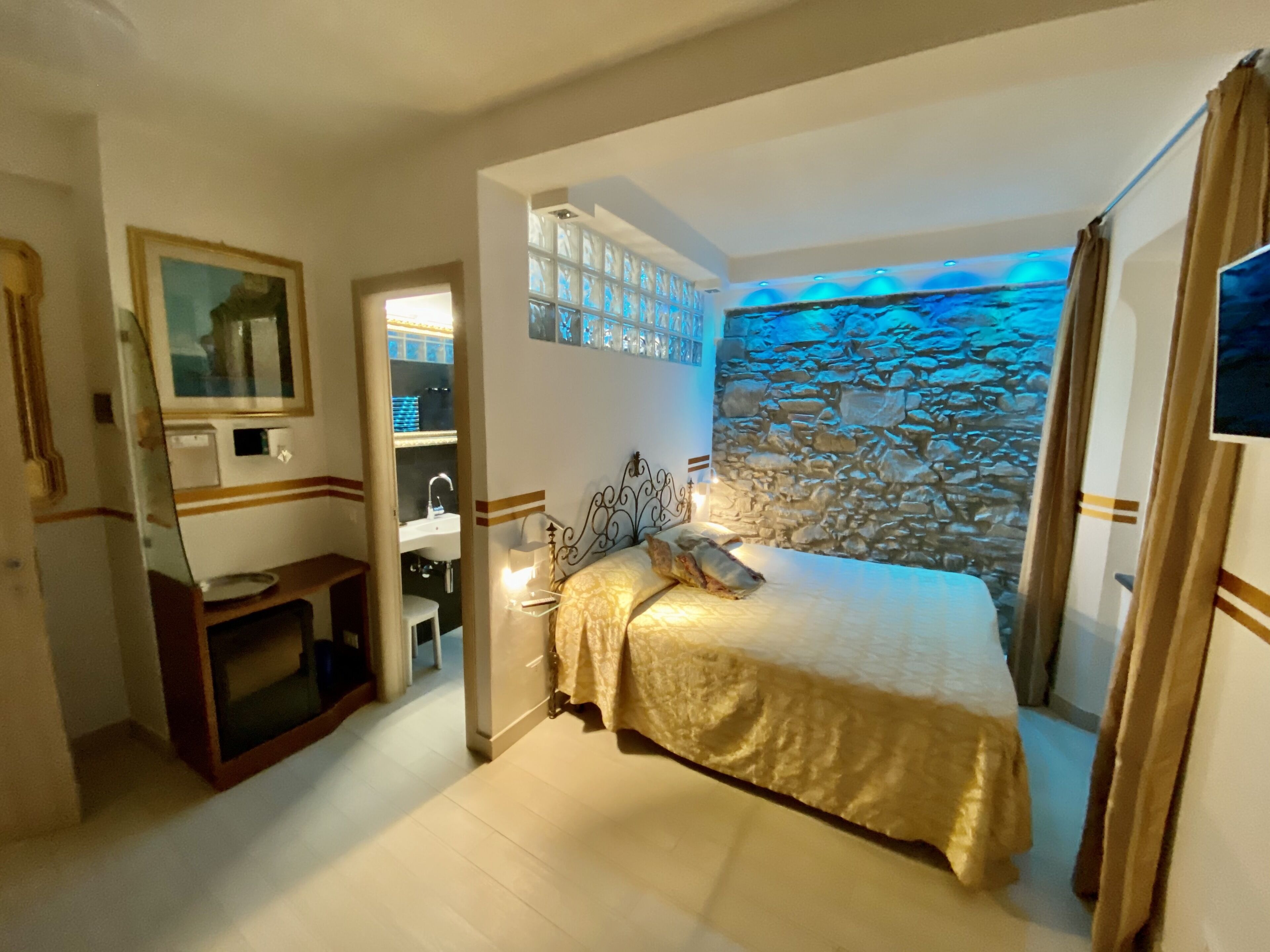 A bedroom with a bed, a mirror, a sink, and a stone wall.