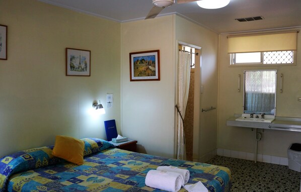 A hotel room with a bed, a desk, a bathroom with a sink and mirror, and a ceiling fan. - Avocado Motor Inn (Childers)