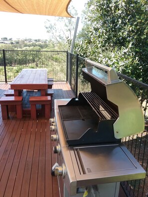 Een barbecue met een tafel en bankjes op een houten terras.