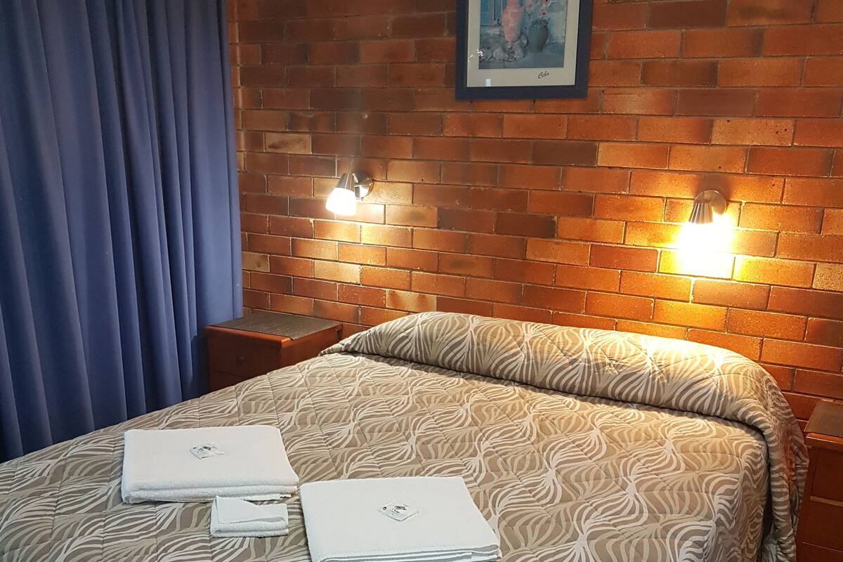 Une chambre d’hôtel avec un mur en briques, une couvre-lit à motifs zébrés, deux serviettes pliées et deux lampes fixées au mur.