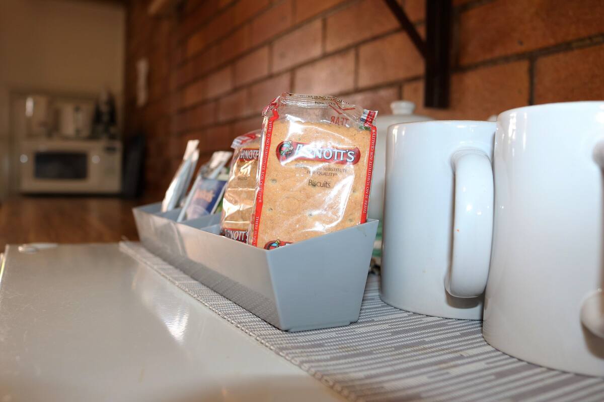 Un plan de travail de cuisine avec une boîte à pain contenant des biscuits, une tasse blanche et un four à micro-ondes en arrière-plan.