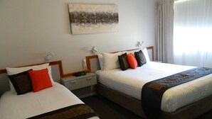 A hotel room with two beds, a nightstand, a lamp, and a painting on the wall. - Orana Windmill Motel (Gilgandra)