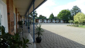 A covered outdoor area with a brick building, potted plants, and a paved walkway. - Orana Windmill Motel (Gilgandra)